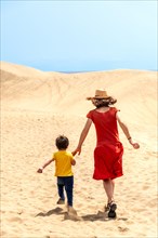 Mother and son tourists enjoying running in the dunes of Maspalomas, Gran Canaria, Canary Islands