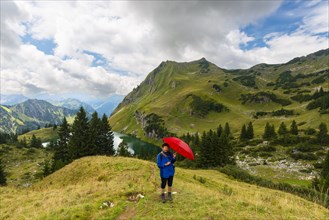 Woman 60-65 hiking with umbrella, behind her Seealpsee and Seekoepfel, 1919m, Allgaeu Alps,