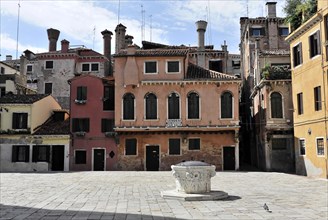 An empty square surrounded by colourful historic buildings in Italy, with a fountain in the middle,