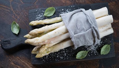 White asparagus on a chopping board with basil and a pinch of salt, bunch of white asparagus