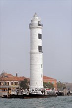 Island of Murano, A white lighthouse stands on the water with a small boat nearby, Venice, Veneto,