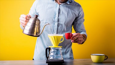 Man with kettle pouring water into a pour-over coffee maker against a vibrant yellow background,