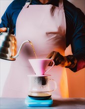 Person with apron manually brewing coffee, pouring water from kettle into a coffee filter, Vertical