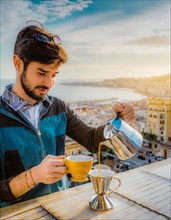 A focused man pours hot water for coffee on a balcony, with a serene sea view in the warm morning