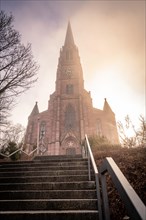 Sunbeams illuminate a church accessible via a staircase with metal railing, sunrise, Nagold, Black