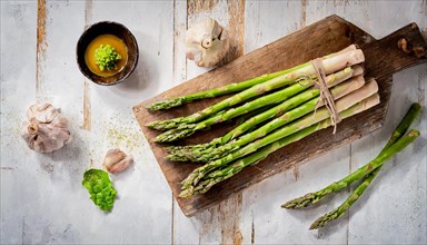 Bundles of asparagus on an old wooden board with garlic and dressing, green asparagus, asparagus