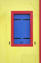 Colourful houses, Burano, Burano Island, Bright yellow wall with blue shutters and a red frame,