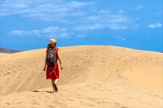 Tourist woman wearing a red dress enjoying in the dunes of Maspalomas, Gran Canaria, Canary Islands