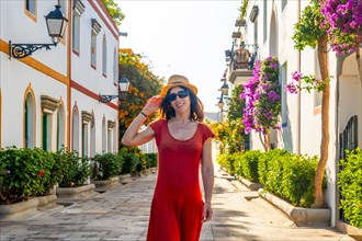 A woman walking in a red dress in the port of the flower-filled coastal town Mogan in the south of