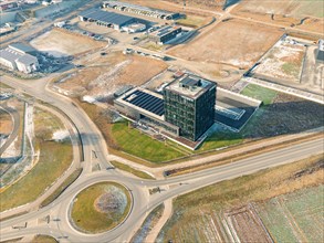 Drone shot of a modern office complex next to roundabout and surrounding fields in industrial area,