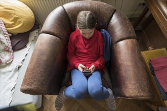 Symbol photo mobile phone, internet, addiction, little girl, 10 years old, sitting in an armchair