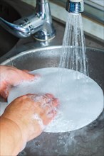 Hands, sink and washing dishes with a person in the kitchen of a home to wash a plate for hygiene.