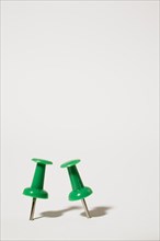 Close-up of two upright green plastic and chrome pushpins on white background, Studio Composition,