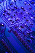 Close-up of blue purple lighted electronic computer circuit board with silver solder points, Studio