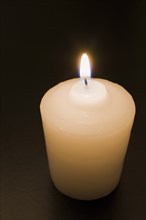 Close-up of white wax candle with bright lit flame on black background, Studio Composition, Quebec,