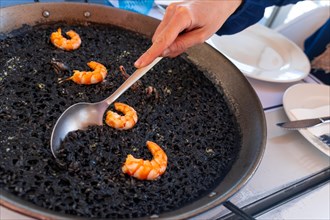 A spoon serving black rice with prawns and squid, a dry rice, cooked in paella or in a clay pot, a