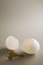 Close-up of antique brass key and two white cracked opened chicken egg shells on grey background,