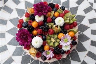 A colourful fruit cake with fresh berries and flowers on a patterned background, Germany, Europe