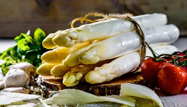 Bundled white asparagus against a rustic background with cherry tomatoes and herbs, fresh white