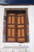 Old brown and orange painted wooden entrance doors on exterior of white roughcast cladded