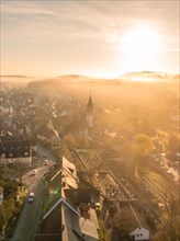 Warm morning light falls on a small town with a visible church tower through the fog, Gechingen,
