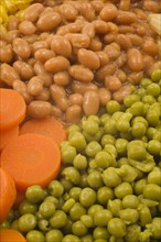 Close-up of mixed cooked vegetables that include brown baked beans, green peas and orange carrots,