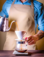 A tattooed arm expertly pours hot water for coffee brewing, highlighting the maker's focus,