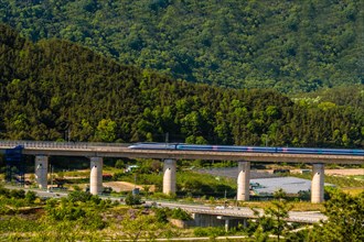 Morning view of a train crossing a bridge with lush mountains in the background, in South Korea