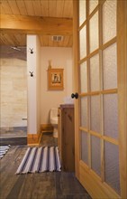 Opened frosted glass French door of main bathroom with tan and dark grey ceramic tile floor and