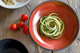 Fresh zucchini noodles with pesto on a red plate garnished with pine nuts and tomatoes, AI