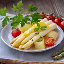 A plate of fresh asparagus and potatoes, garnished with cherry tomatoes and parsley on a wooden