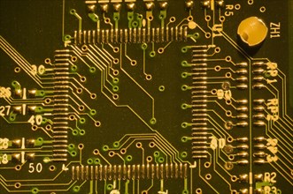 Close-up of microchip, silver solder points and lines on golden lighted electronic computer circuit
