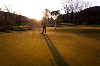 Male Golfer Concentration on the Putting Green on Golf Course in Sunset with Shadow in Switzerland.