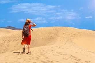 Tourist woman wearing a red dress enjoying in the dunes of Maspalomas, Gran Canaria, Canary Islands