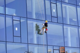 Marseille harbour, window cleaner secured by ropes to a reflective glass facade of a tall building,