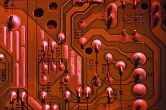 Close-up of red lighted electronic computer circuit board with silver solder points, numbers and