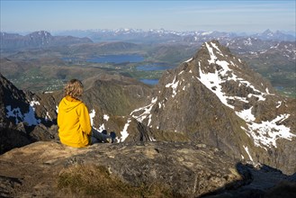 Mountain landscape in the Lofoten Islands. A hiker sits on the summit of Himmeltindan mountain and