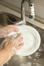Close-up of a woman washing dishes in the kitchen sink with a scouring sponge full of soap and soap
