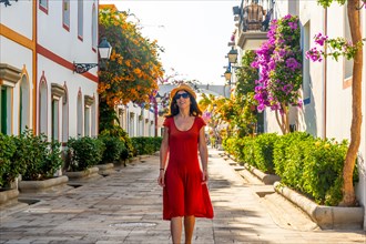 A woman walking in a red dress in the flower-filled port of Mogan town in the south of Gran Canaria