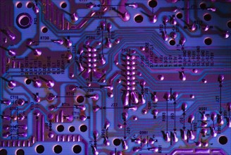 Close-up of purple and blue lighted electronic computer circuit board with silver solder points and