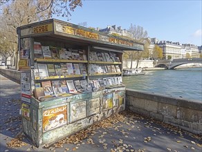 Ein traditioneller Zeitschriftenstand am Flussufer mit herabfallenden Herbstblaettern im