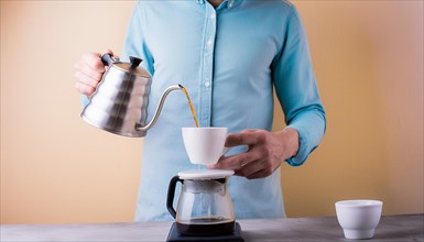 Man in a blue shirt focused on pouring hot water from a gooseneck kettle into a coffee filter,