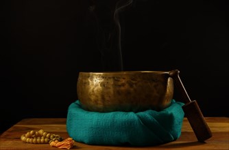Tibetan singing bowl smoking on green cloth next to a Buddhist japa mala isolated on black