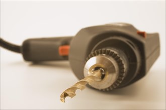 Close-up of electric drill with black power cord and titanium bit on white background, Studio