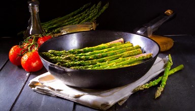 Dark, atmospheric shot of asparagus in a pan next to fresh tomatoes, green asparagus, asparagus