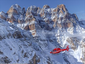Roter Hubschrauber im Flug nahe schneebedeckten Felsformationen und Wolken, Rettungshubschrauber im