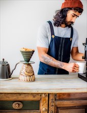 A tattooed barista manually brews coffee, demonstrating individuality and a vintage vibe, Vertical