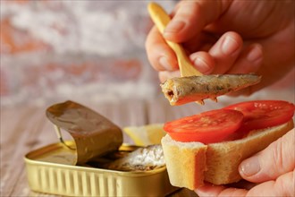 A woman puts a sardine on a slice of bread with tomato, in the background you can see the can of