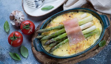 Fine asparagus gratin garnished with fresh cherry tomatoes and garlic on a wooden base, asparagus