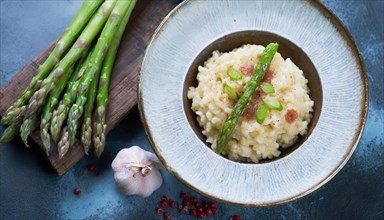 A plate of risotto with asparagus and pieces of bacon next to garlic cloves, risotto with green